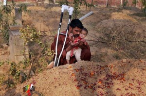 Mohammed Tofeeq carga a su hija de 10 meses, Gulshan Tofeeq, mientras reza frente a la tumba de su esposa Muqadas Tofeeq, quien de acuerdo con la policía local fue asesinada por su madre en la aldea de Butrawala en las afueras de Gujranwala, Pakistán, el sábado 18 de junio de 2016. (AP Foto/K.M. Chaudary)